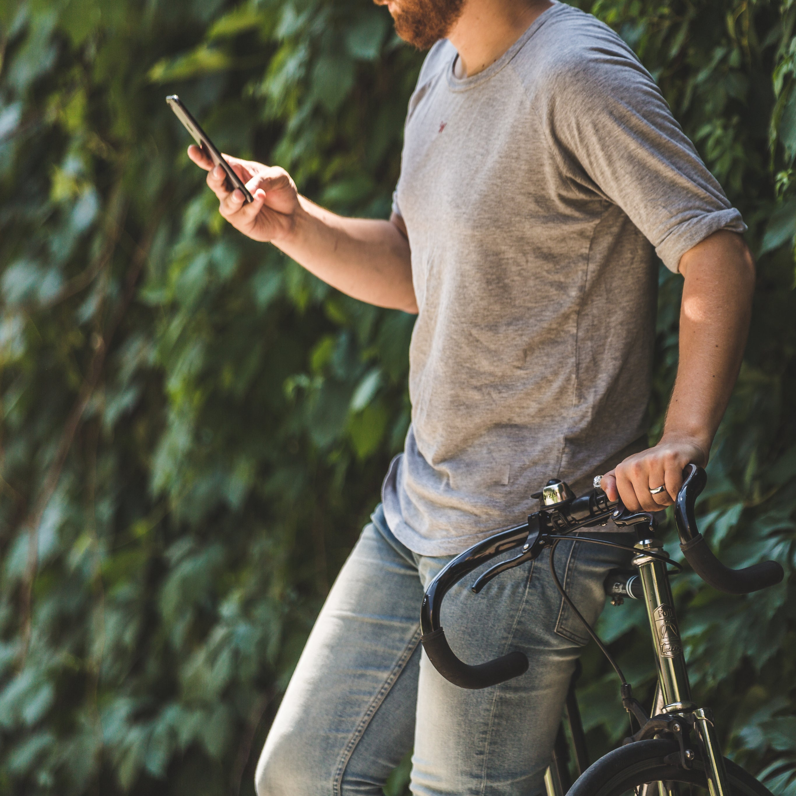 Authentisches Social Media Marketing: Mann auf dem Fahrrad nutzt Smartphone in entspannter, grüner Umgebung – geschmacksRaum® WERBEAGENTUR
